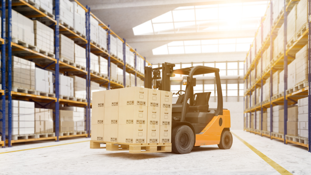 倉庫内でフォークリフトがパレット積みの段ボール箱を安定して運搬しており、整理整頓された保管棚と十分な作業スペースの中で安全に荷役作業が行われている様子を示す