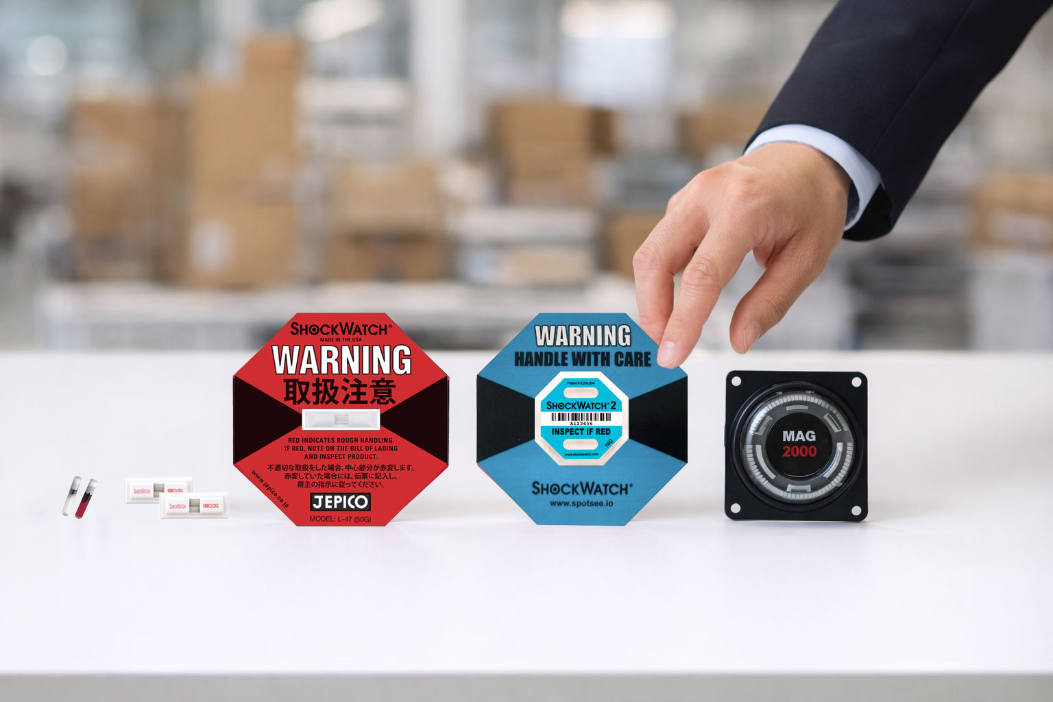 複数種類の衝撃検知ラベルやインジケーターを並べ、手で選択している様子から用途や感度に応じた選び方を示している構図